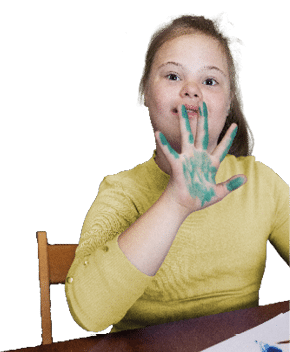 Una persona joven con cabello recogido y su ter amarillo muestra una mano con pintura verde mientras est sentada en una silla junto a una mesa.  Descripci n generada con IA