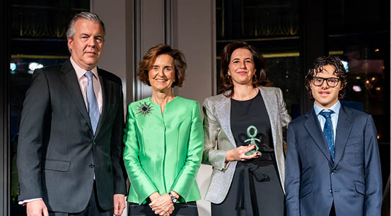 Dos personas vestidas con trajes elegantes, una con un vestido verde liso y la otra con un saco brillante plateado. Descripci n generada con IA
