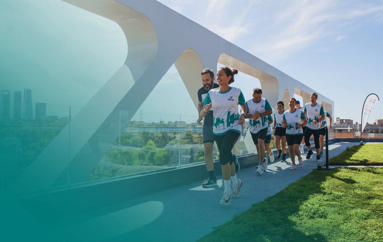 Un grupo de personas con camisetas deportivas corre en un camino al aire libre junto a una estructura blanca moderna bajo un cielo despejado. Descripci n generada con IA