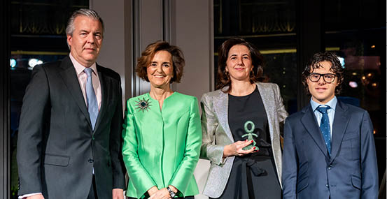 Dos personas vestidas con trajes elegantes, una con un vestido verde liso y la otra con un saco brillante plateado. Descripci n generada con IA